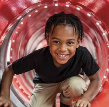 Child crawling through a red tunnel in the indoor playground